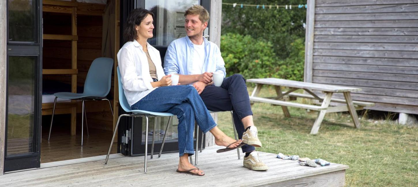 Paar sitzt und unterhält sich vor einer Hütte auf dem Zeltplatz von Tunø in der Urlaubsregion Küstenland