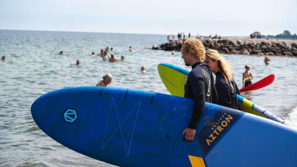 Et par har SUP boards under armen og går ud i vandet på Storstranden i Juelsminde
