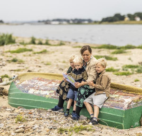 Eine Frau sitzt mit drei kleinen Jungen mit einer Schatzkarte am Strand